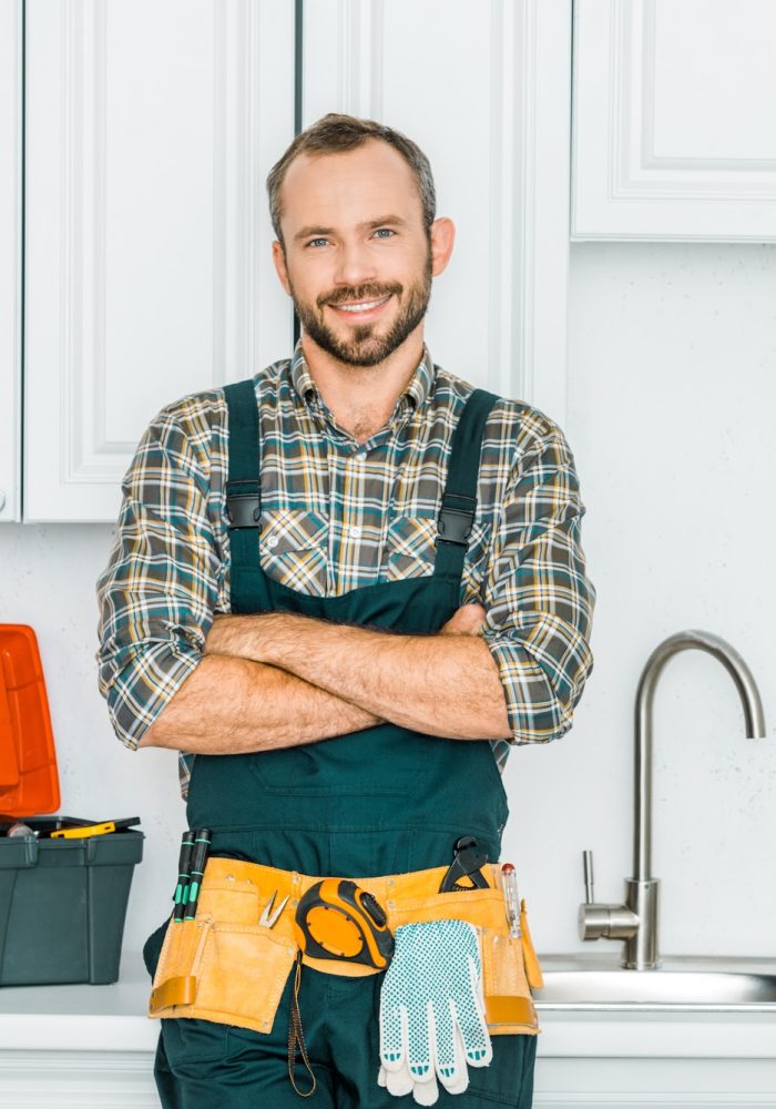 smiling-handsome-plumber-standing-with-crossed-arms-and-looking-at-camera-in-kitchen.jpg